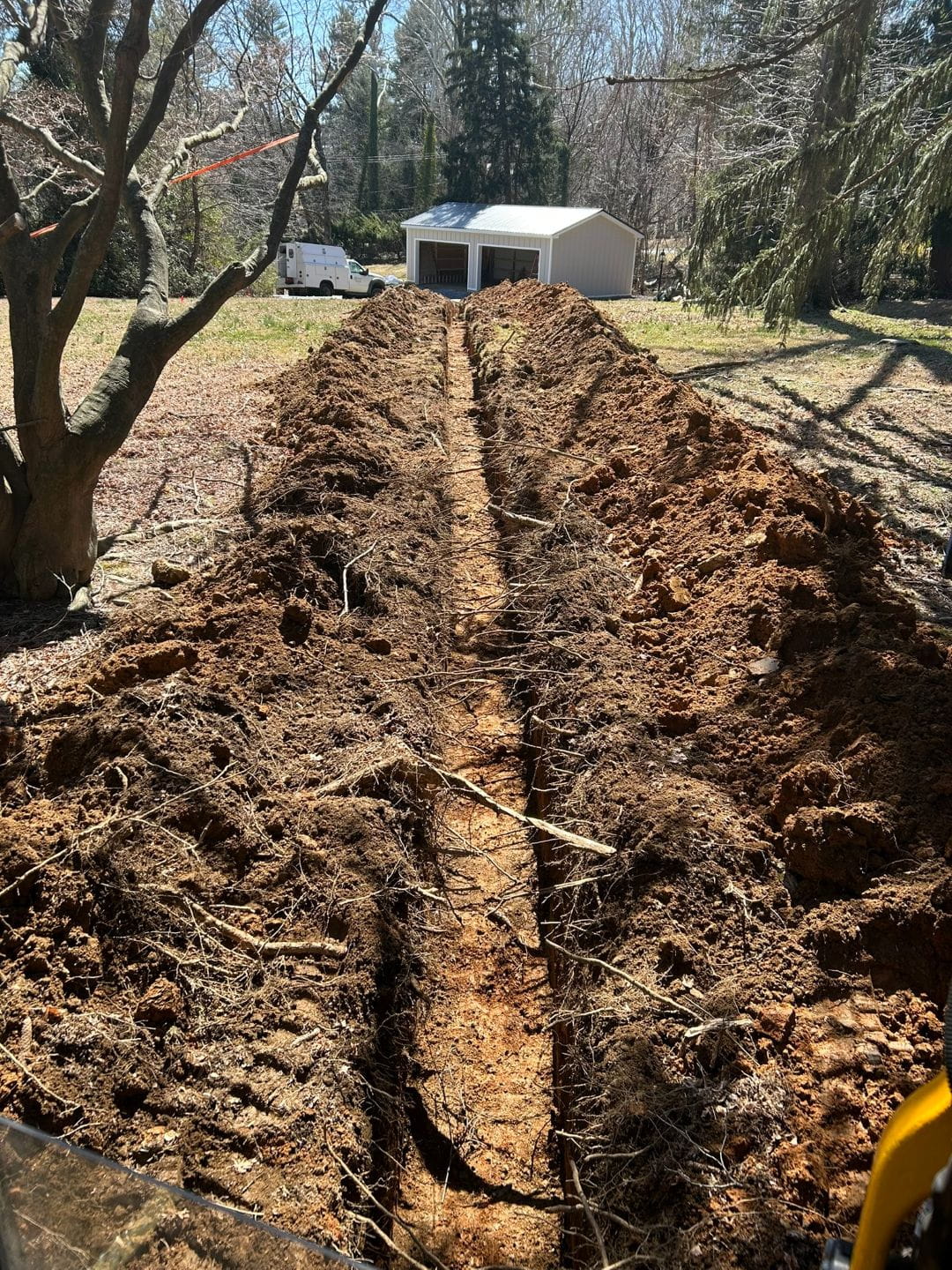 Long-distance utility trench excavation across a residential property.