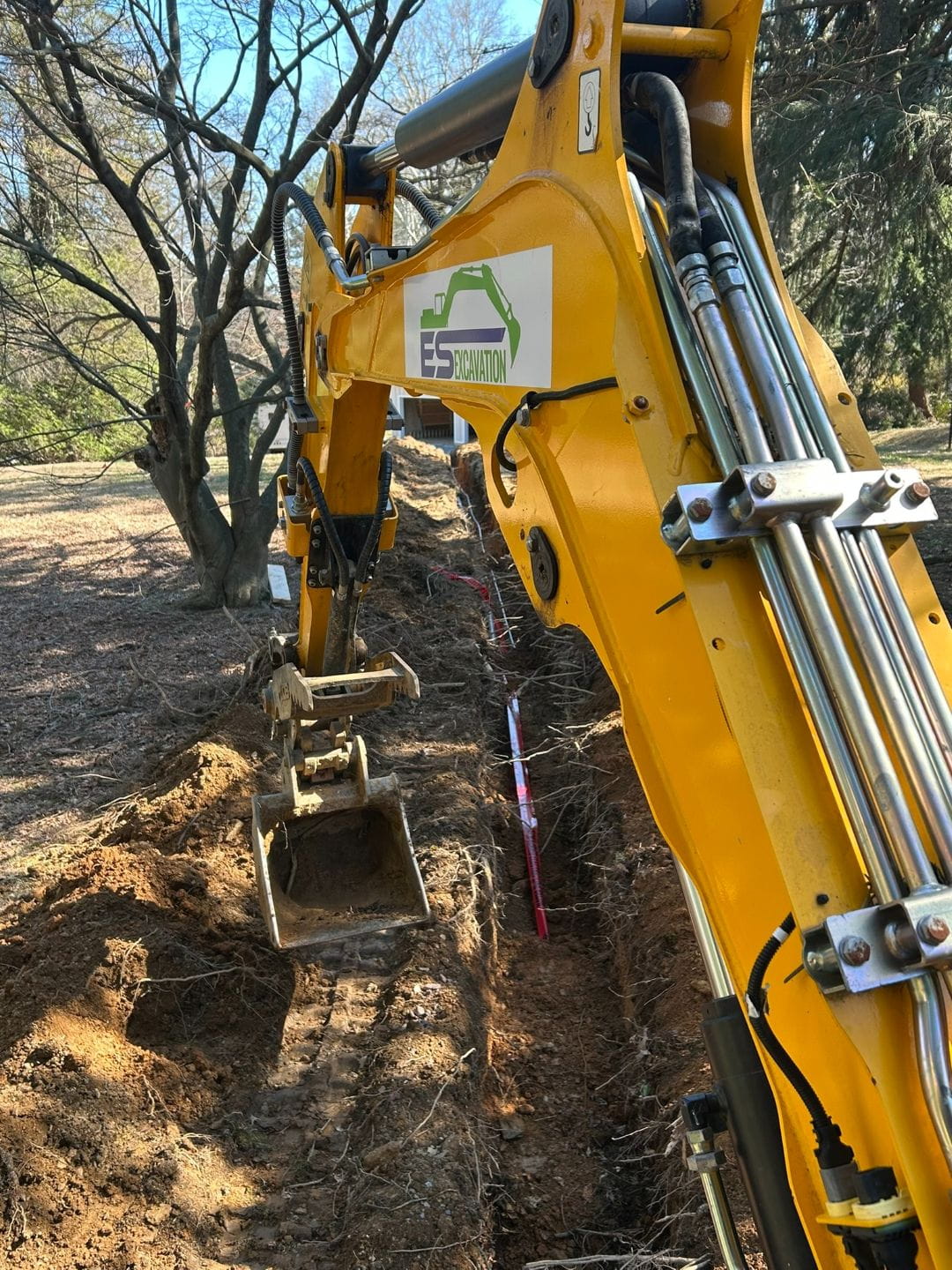 Mini excavator trenching for underground utility installation on a residential property.