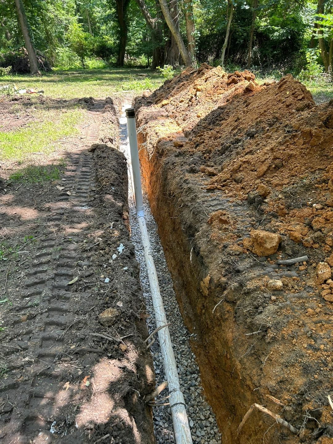 Residential sewer line installation with PVC pipe placed in stone bedding.