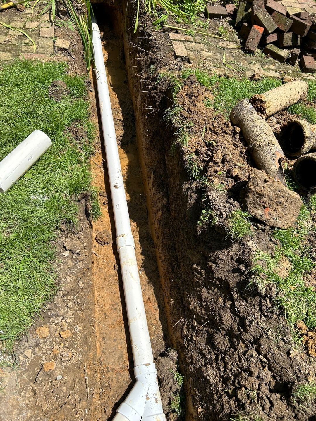 Residential sewer line installation with PVC pipe placed in an excavated trench.