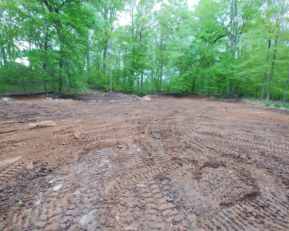 Cleared land with tire tracks surrounded by lush green trees.