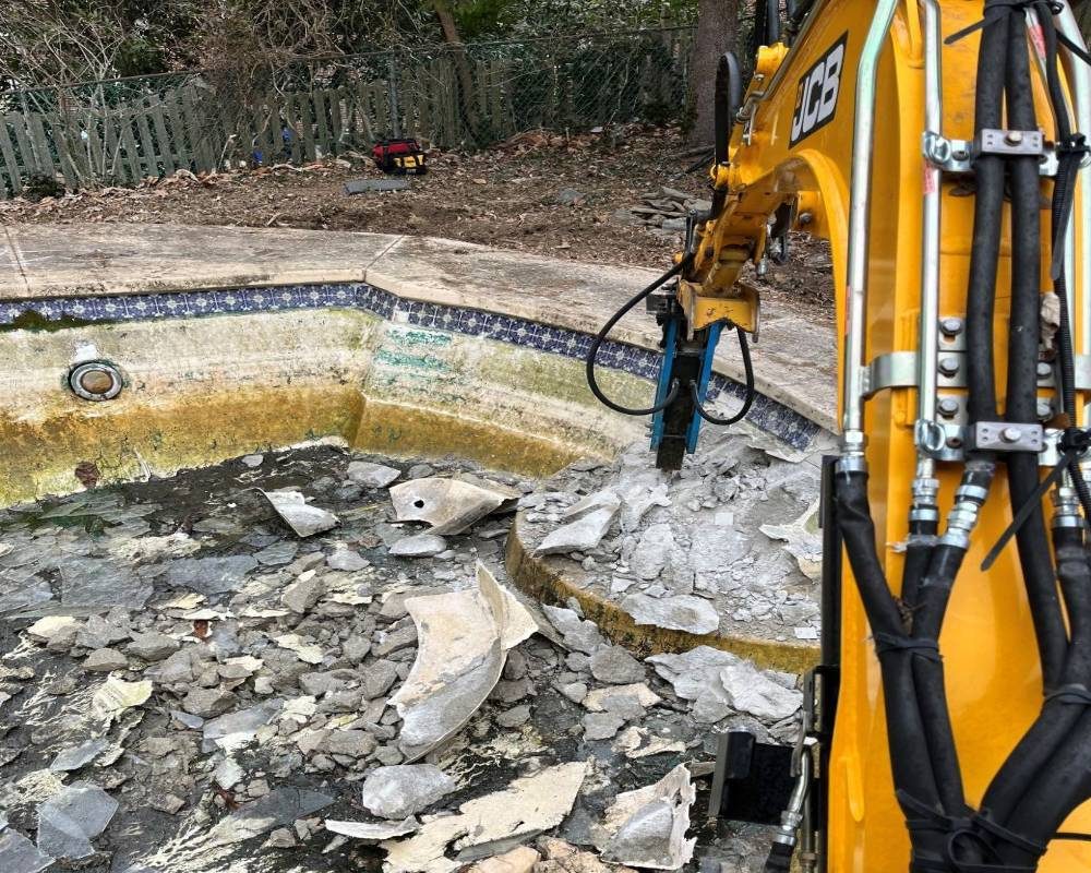 Excavator removing concrete materials during residential swimming pool demolition project.