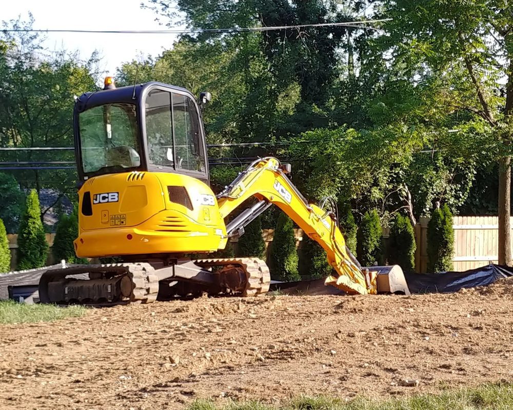 Yellow mini excavator working on a dirt patch near trees.