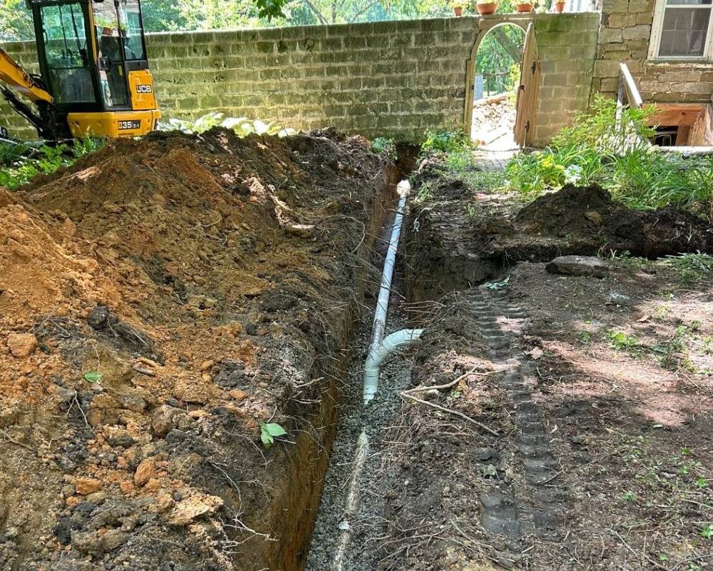 Residential sewer line installation with trench excavation, stone bedding, and underground utility work.